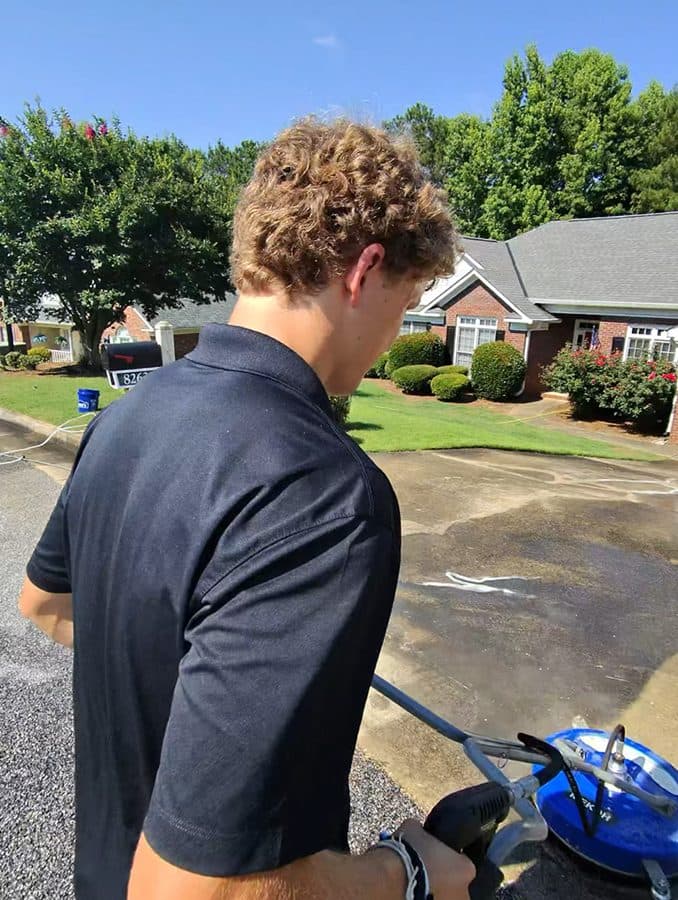 Team Clean worker using a pressure washing surface cleaner on a driveway